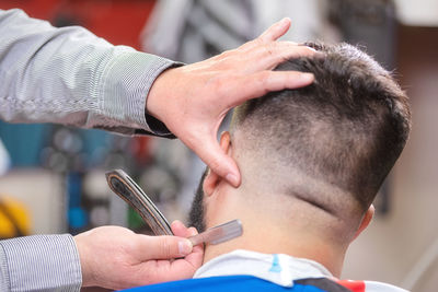 Cropped hands of barber cutting male customer hair in salon