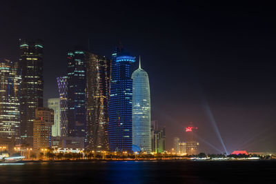 Illuminated city by buildings against sky at night