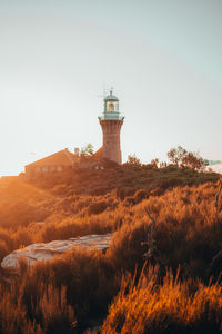 Lighthouse on field by building against sky