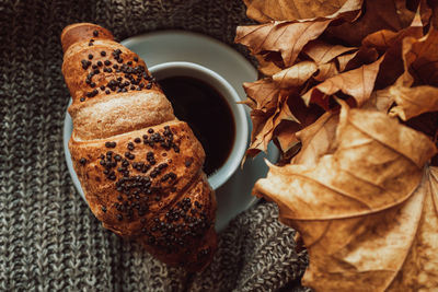 A cup of black morning coffee with a chocolate croissant in a cozy autumnal still life