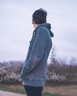 Side view of young man standing on field against sky