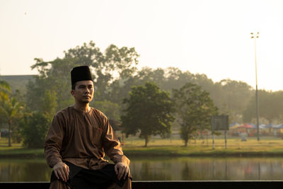 Young man looking away while standing against sky