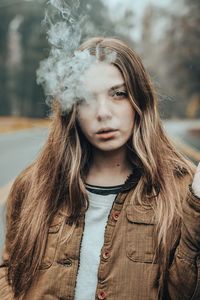 Portrait of beautiful young woman smoking while standing on road