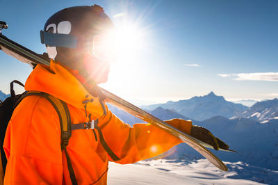 Rear view of man standing on snow covered mountain against sky during sunset