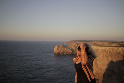 Woman with hand in hair against sea during sunset