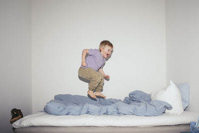 Carefree boy jumping on bed against wall at home