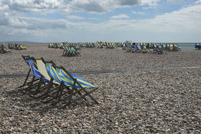 Deck chairs on beach against sky