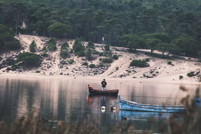 Mid distance view of man standing on rowboat in lake