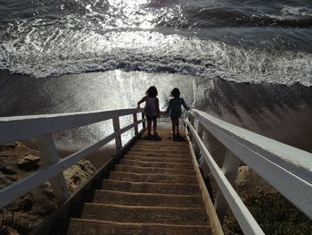 High angle view of girls walking on steps leading towards sea during sunny day