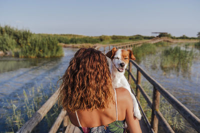 Rear view of woman with dog on footbridge against sky