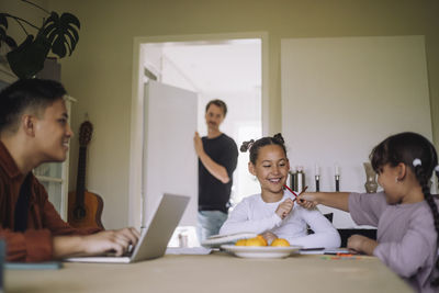 Smiling sisters playing with pencils while sitting at table in home