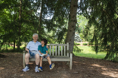 Grandfather with grandson sitting on bench against trees at park