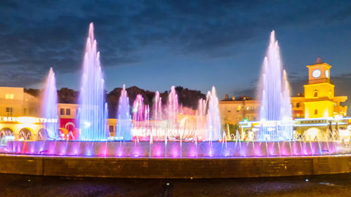 Illuminated fountain in city against sky at night