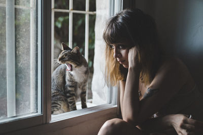Young woman sitting by window with cat at home