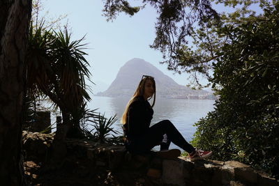 Woman sitting by tree against sky