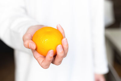 Girl in a white sweater holds a fresh sweet tangerine against the background of herself in defocus