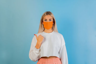 Portrait of beautiful young woman wearing mask gesturing against blue background