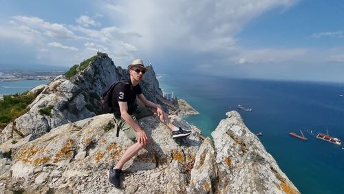 Rear view of man sitting on rock against sky