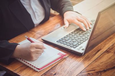 Midsection of woman with book and pen using laptop on table