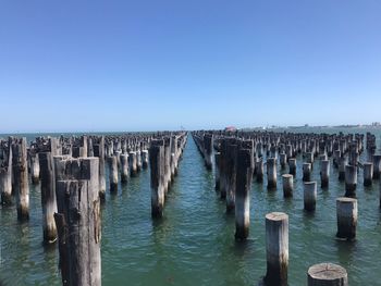 Wooden posts in sea against clear blue sky