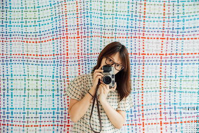 Portrait of mid adult woman photographing with camera against textile