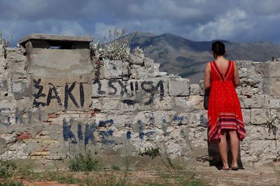 Full length rear view of woman standing by wall outdoors