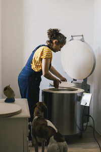 Side view of female craftsperson putting ceramic plate in electric kiln while working at home