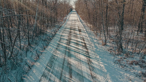 Elevated view of a snow covered dirt road in the forest. the sun shines through the trees.