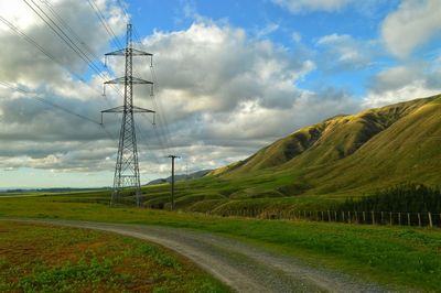 Electricity pylon on field against cloudy sky