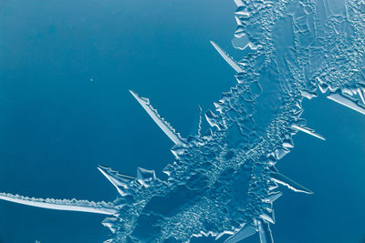 Low angle view of snowflakes on glass against blue background