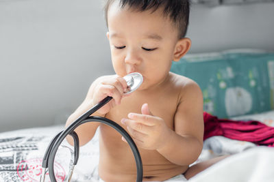 Cute baby boy holding stethoscope while sitting on bed at home