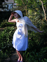 Woman in scarf and dress shielding eyes while standing against plants