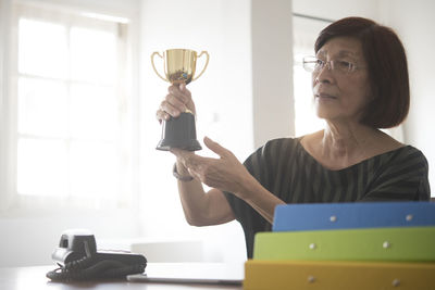 Thoughtful woman looking away while holding trophy at office