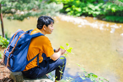 Smiling man sitting by lake during sunny day