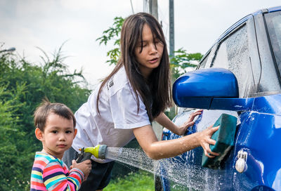 Full length of mother and son cleaning car outdoors