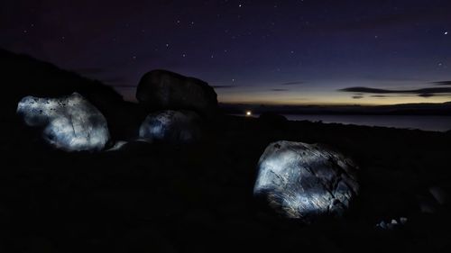 Rocks by sea against sky at night