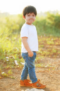 Side view portrait of boy standing on field during sunset