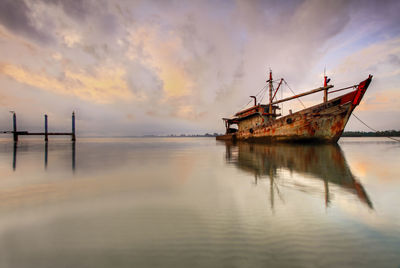 Abandoned ship in sea against sky during sunset