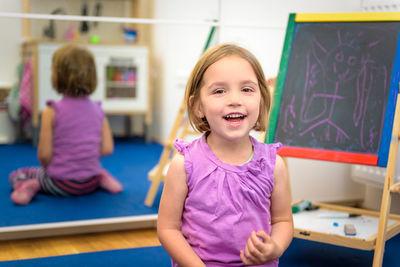 Close-up portrait of happy girl kneeling against mirror with reflection at home