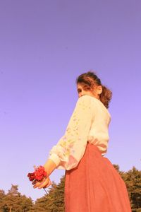 Rear view of women standing by flowering plant against clear sky