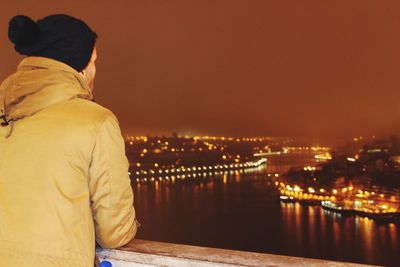 Man looking at illuminated cityscape against sky at night