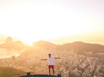 Rear view of woman standing on city against sky during sunset