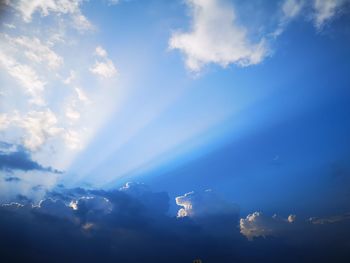 Low angle view of sunlight streaming through clouds