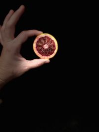 Cropped hand holding lemon slices against black background