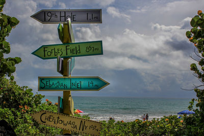 Information sign by sea against sky