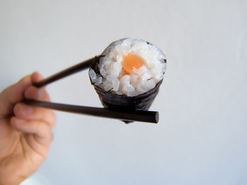 Close-up of hand holding sushi against white background