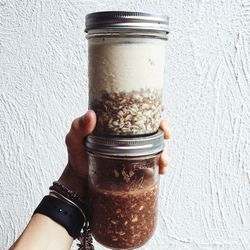 Cropped hand holding chia smoothie jars against white wall