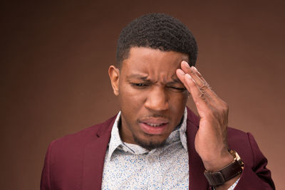 Young man with headache against brown background