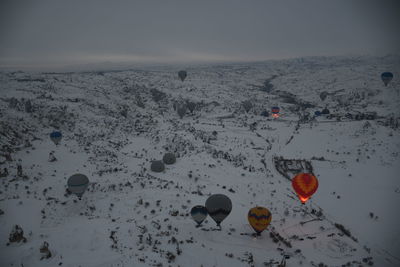 High angle view of hot air balloons flying over snow covered landscape