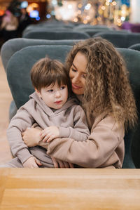 Little boy child is sitting on his mother's lap in a shopping and entertainment center in a food